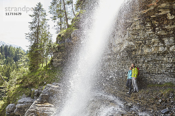 Junges Paar steht unter einem Wasserfall und schaut hinaus  Tirol  Österreich