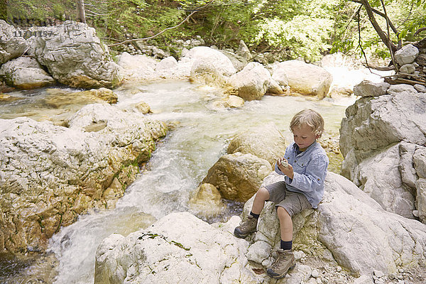 Junge sitzt auf Felsen am Waldfluss  Bovec  Soca  Slowenien