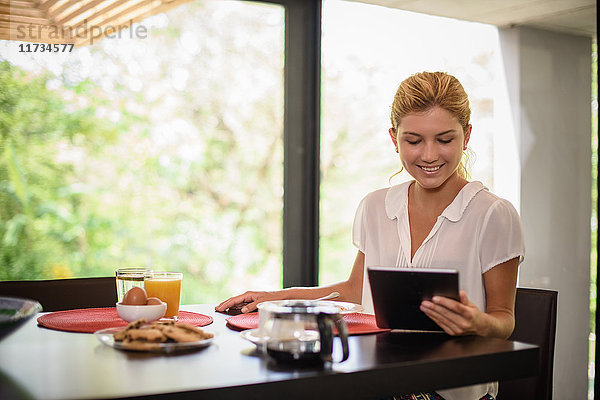 Junge Frau am Frühstückstisch beim Durchstöbern des digitalen Tablets
