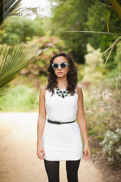 Junge Frau in weißem Kleid und Sonnenbrille im Park