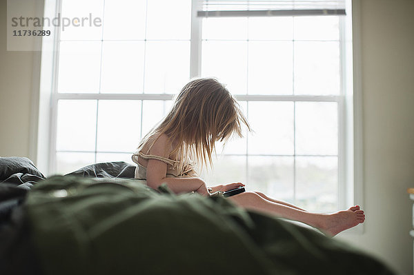 Mädchen sitzt auf dem Bett und benutzt ein Smartphone