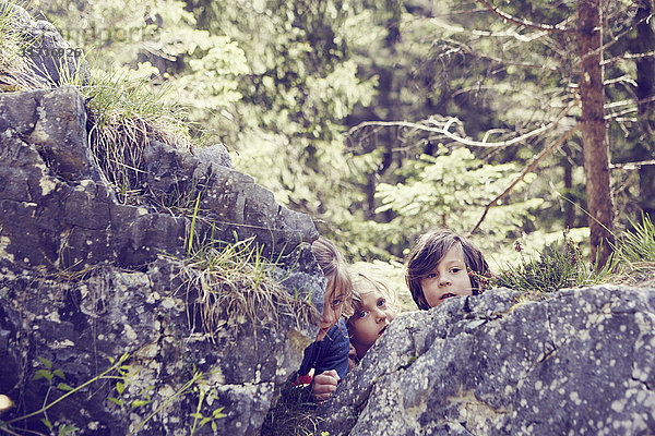 Drei Kinder verstecken sich hinter Felsen im Wald