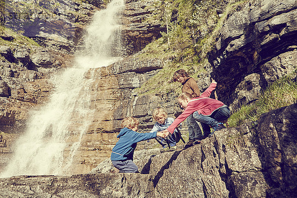 Gruppe von Kindern klettert an Felsen neben dem Wasserfall