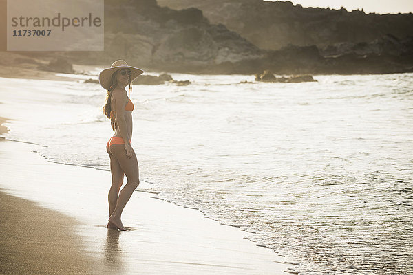 Mittlere erwachsene Frau mit Sonnenhut und Bikini am Strand stehend  Maui  Hawaii  USA