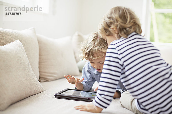 Zwei Jungen sitzen auf dem Sofa und benutzen ein digitales Tablett