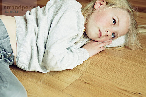Junges Mädchen liegt auf Holzboden und schaut weg