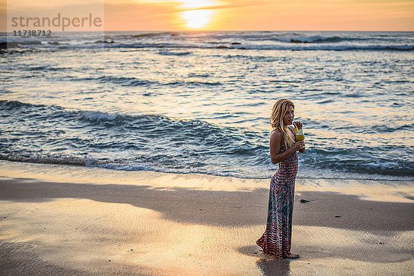 Porträt einer jungen Frau  die bei Sonnenuntergang am Strand einen Cocktail trinkt  Tamarindo  Costa Rica