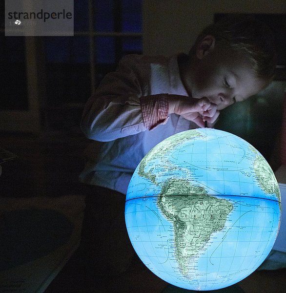 Junge blickt auf beleuchteten Globus in dunklem Raum