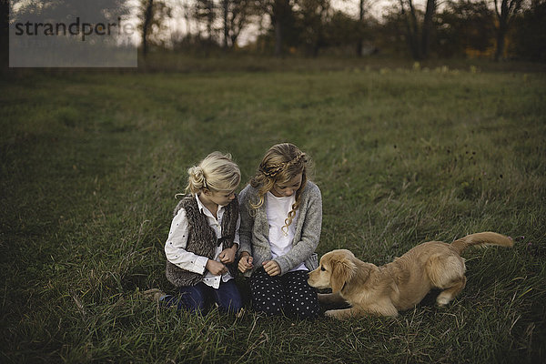 Zwei junge Mädchen sitzen mit ihrem Hund auf dem Feld