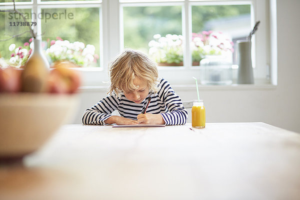 Junge Junge sitzt am Tisch und schreibt