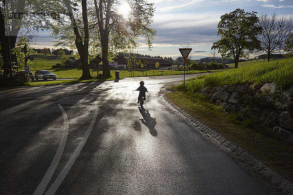 Hintere Silhouettenansicht eines Jungen  der auf einer Landstraße Fahrrad fährt