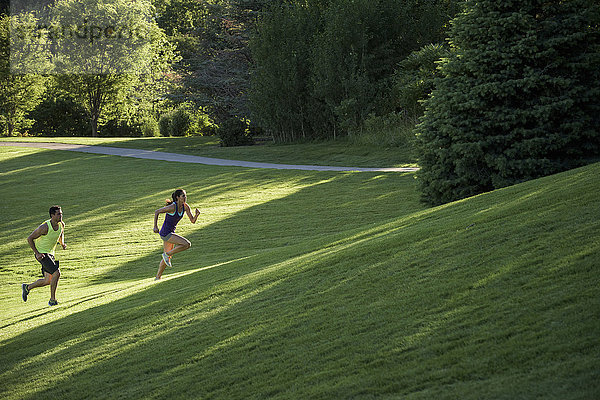 Junger Mann und Frau machen Trainingsläufe auf einem Hügel im Park
