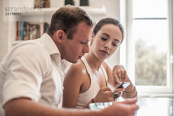 Junges Paar betrachtet Smartphone am Küchentisch