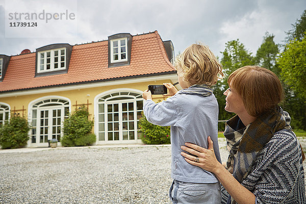 Junge mit einer mittel-erwachsenen Frau  die ein Smartphone benutzt  um ein Haus zu fotografieren