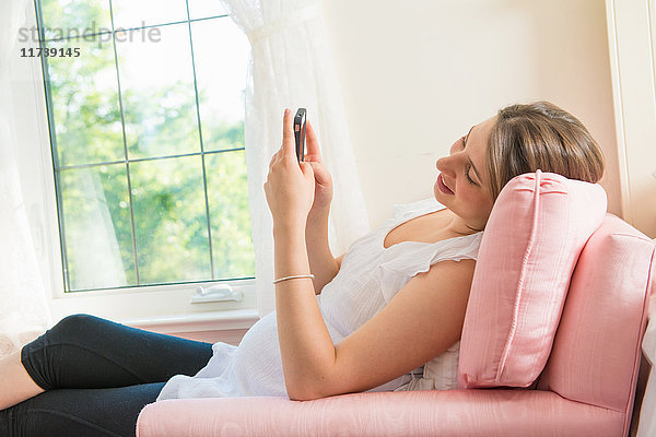 Schwangere  die auf einem Sessel sitzt und ein Smartphone benutzt