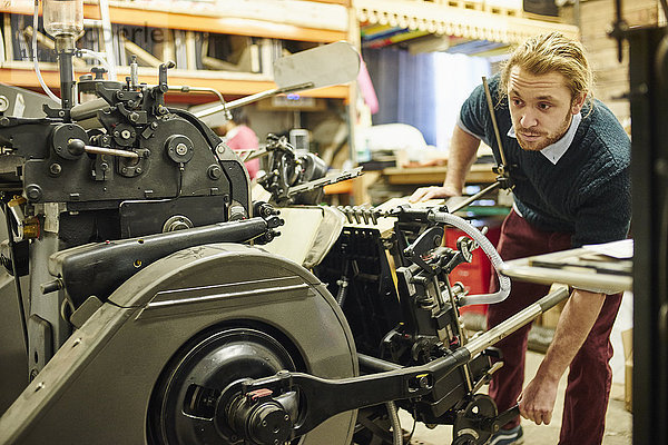 Junger Mann bedient alte Druckmaschine in traditioneller Druckwerkstatt