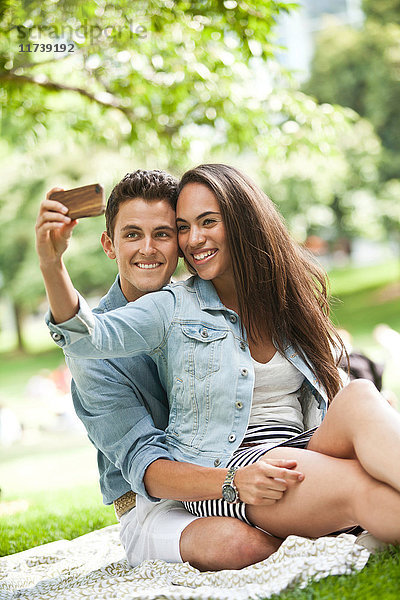 Lächelndes junges Paar  das sich im Park mit einem Fotohandy selbst porträtiert