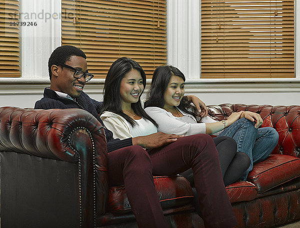 Drei junge erwachsene Freunde sitzen zusammen auf dem Sofa