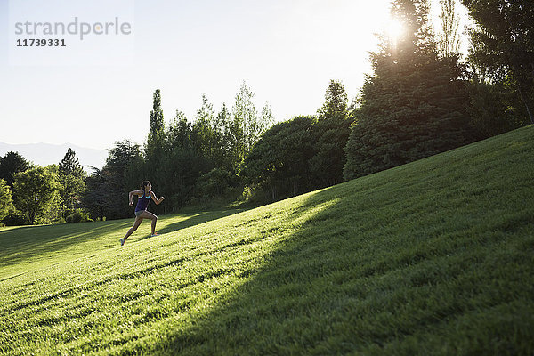 Junge Frau beim Trainingslauf auf einem Hügel im Park