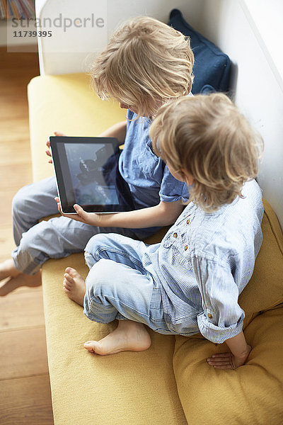 Zwei kleine Jungen sitzen auf einem Sofa und schauen auf ein digitales Tablet