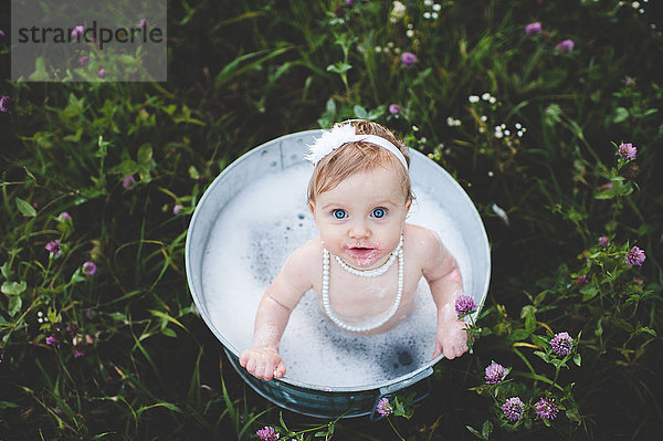Draufsicht auf ein kleines Mädchen  das in einer Blechbadewanne in einer Wildblumenwiese badet