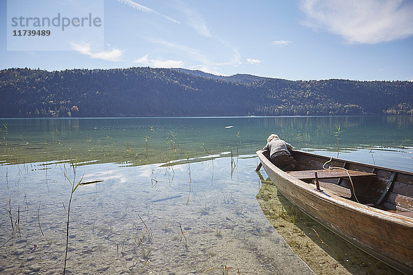 Junge beugt sich vom Ruderboot vor und schaut in den See  Kochel  Bayern  Deutschland