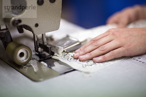 Hände eines männlichen Textildesigners bei der Benutzung einer Nähmaschine in einer alten Textilfabrik
