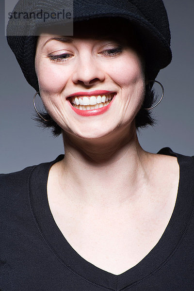 Junge Frau mit schwarzem Hut schaut nach unten und lächelt