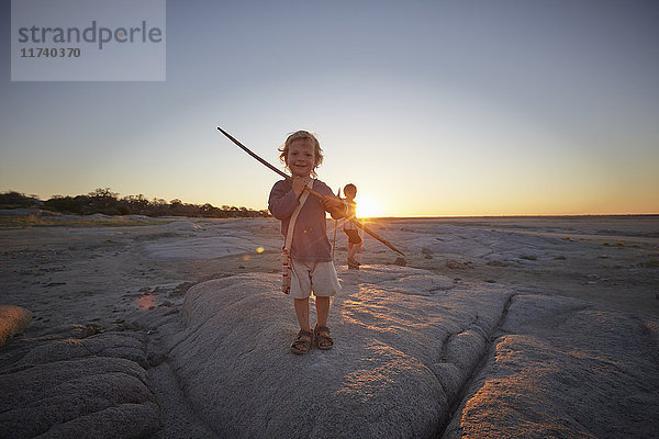 Porträt eines Jungen  der auf einem Felsen steht und einen Speer hält  Sonnenuntergang  Gweta  makgadikgadi  Botswana
