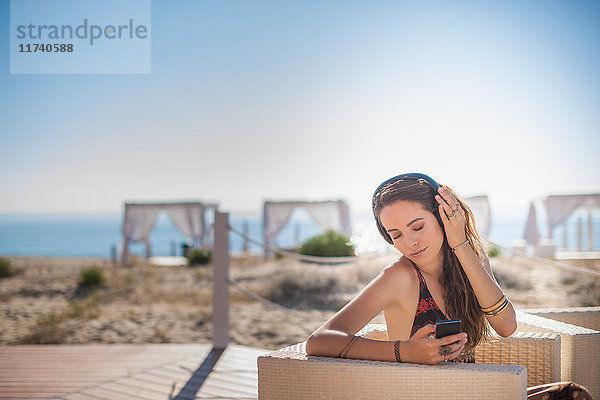 Junge Frau hört Musik über Kopfhörer am Strand  Castiadas  Sardinien  Italien