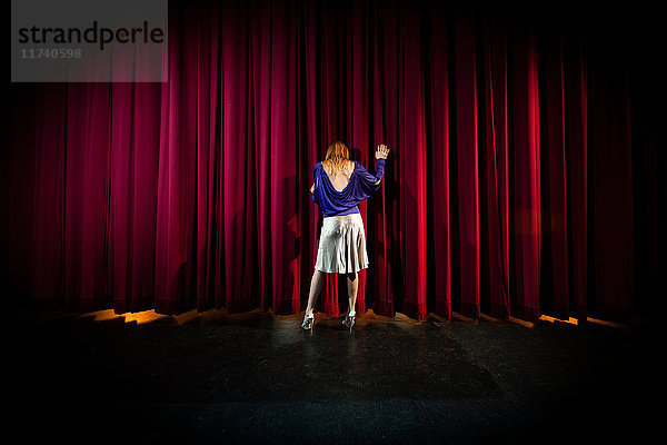 Reife Frau auf der Theaterbühne stehend  Rückansicht