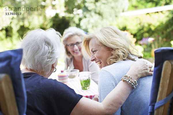 Drei Frauen entspannen sich gemeinsam im Garten und lachen