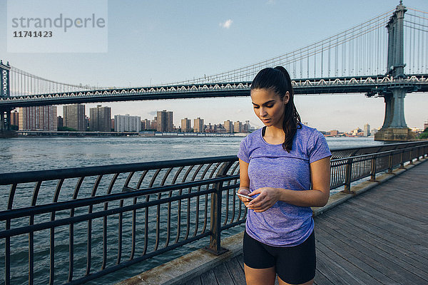 Junge Läuferin liest Smartphone vor der Manhattan-Brücke  New York  USA