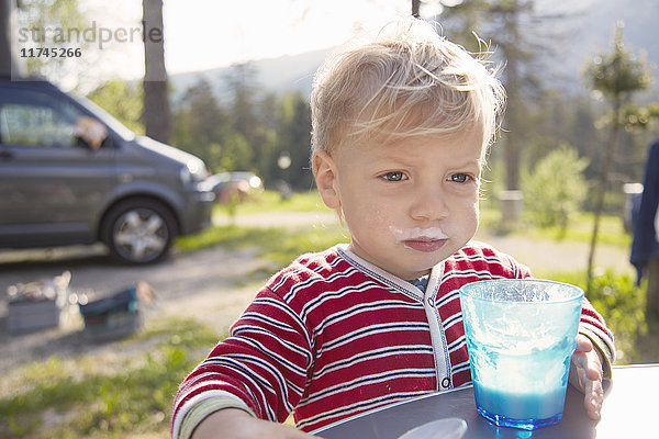 Porträt eines männlichen Kleinkindes  das Milch trinkt  auf einem Waldcampingplatz  Toblacher See  Dolomiten  Südtirol  Italien