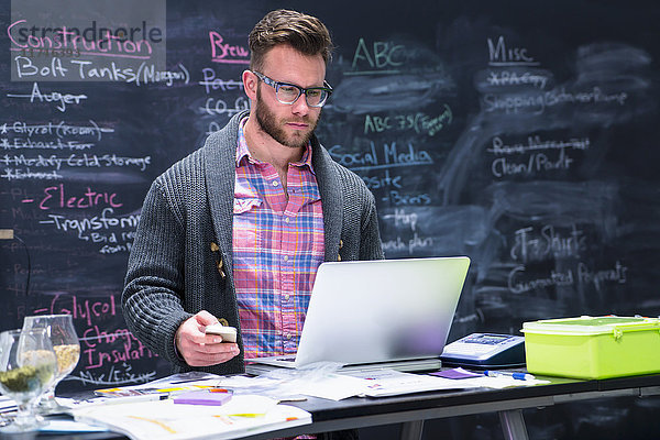 Junger Mann am Arbeitsplatz mit Laptop und Smartphone in der Hand