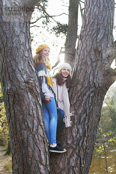 Mädchen im Teenageralter stehen im Baum und schauen lächelnd weg