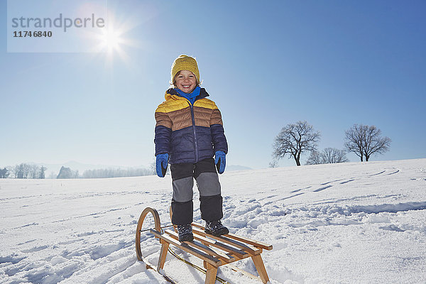 Porträt eines auf einem Schlitten stehenden Jungen in verschneiter Landschaft