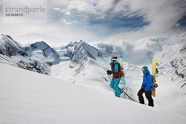 Junge Leute klettern mit Skiausrüstung auf den Gipfel eines Berges