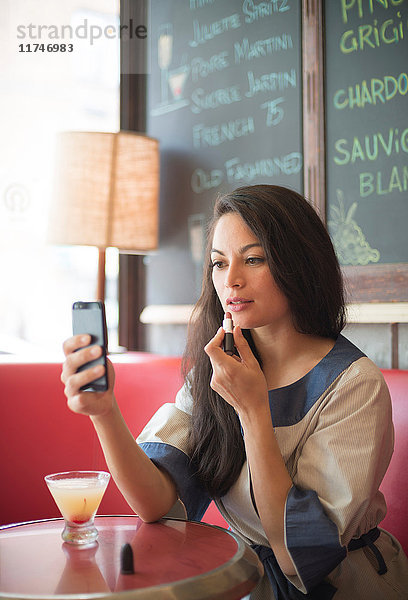 Mittelgroße erwachsene Frauen  die im Restaurant Lippenstift per Handy auftragen