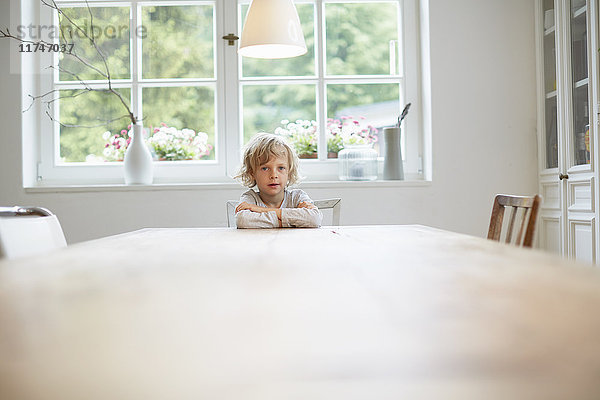 Porträt eines Jungen  der an einem leeren Esstisch sitzt