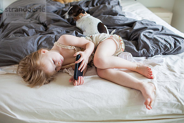 Auf dem Bett liegendes Mädchen mit Smartphone