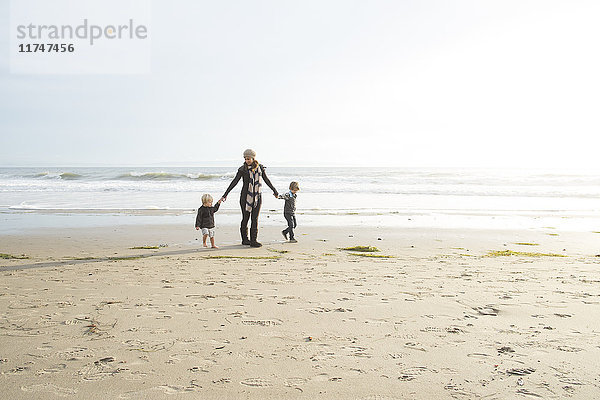 Mutter und zwei Söhne halten am Strand Händchen