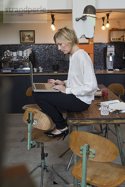 Mittelgroße erwachsene Frau  die mit einem Laptop am Tisch sitzt