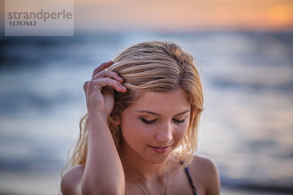 Junge Frau mit Hand im Haar am Strand bei Sonnenuntergang