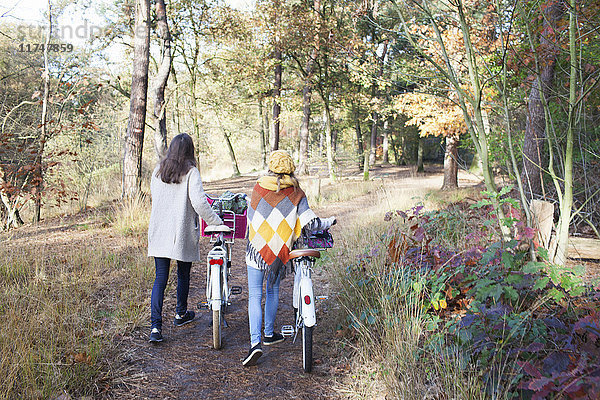 Rückansicht in voller Länge von Teenager-Mädchen  die im Wald laufen und Fahrräder schieben