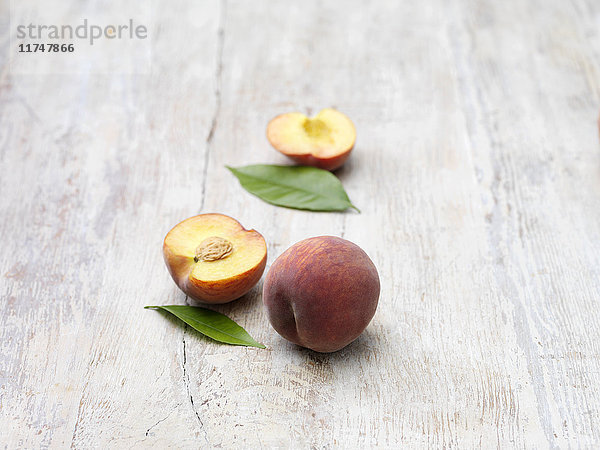 Pfirsiche ganz und halb auf gekalktem Holztisch
