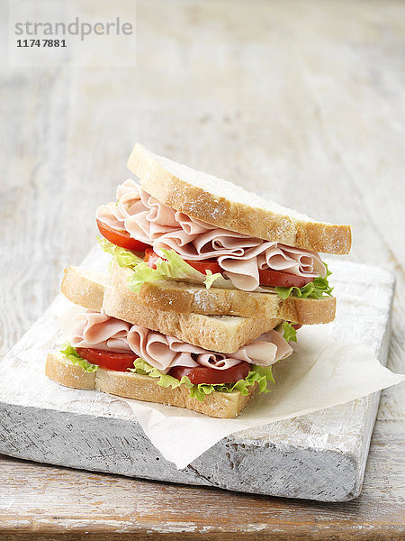 Stapel hauchdünner Schinken-Sandwiches auf geschnittenem Weißbrot mit Salatblättern und Tomaten