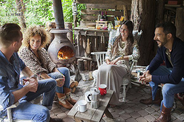 Vier erwachsene Freunde trinken Kaffee in einer offenen Hütte mit Holzofen
