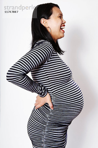 Schwangere Frau im mittleren Erwachsenenalter  die vor weißem Hintergrund lacht