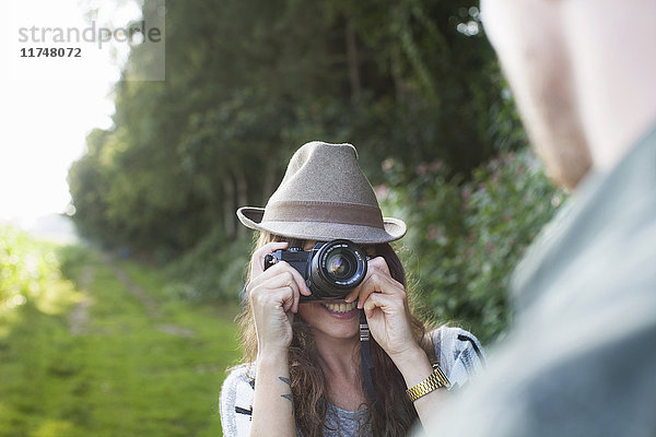 Über-die-Schulter-Ansicht einer jungen Frau  die ihren Freund im Feld fotografiert